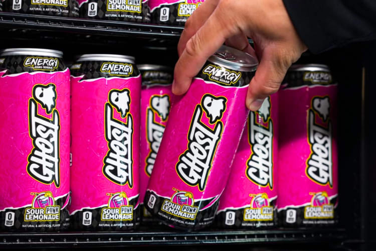 A person taking a pink energy drink from a store refrigerator