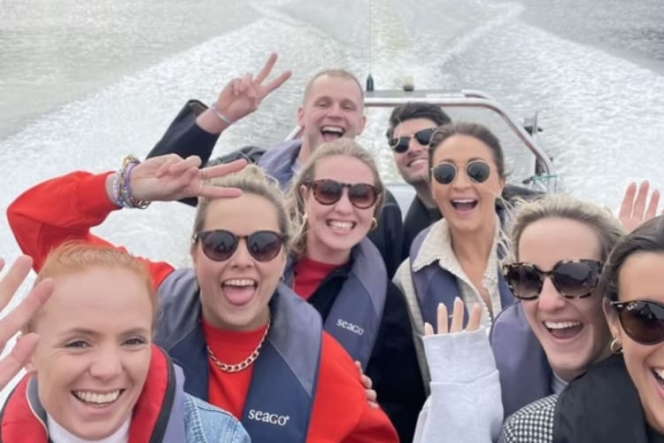 a group smile at the camera on board a high-speed powerboat leaving waves behind them