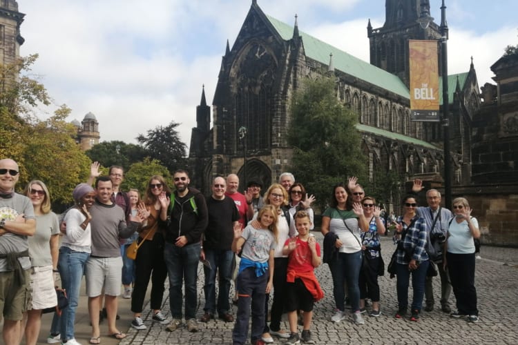 a group of people stand in front of a Glasgow landmark enjoying a walking tour of the city