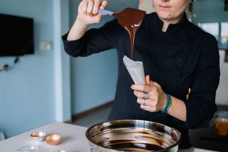 a woman pours liquid chocolate into a piping bag