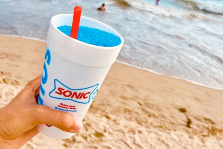 A person holding a blue Sonic slushie at the beach