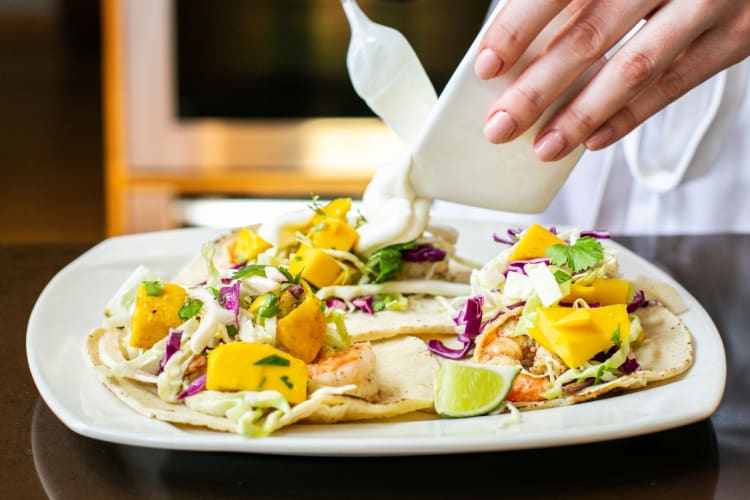A chef plating tacos with shrimp and mango