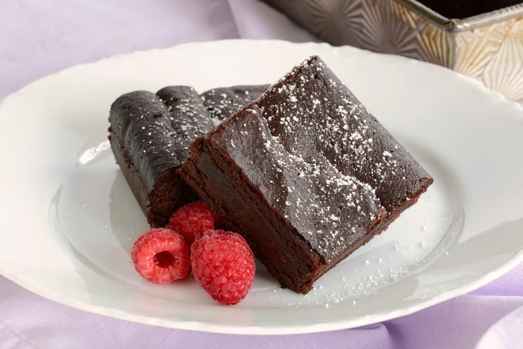 Two brownies on a plate with coconut shavings and raspberries