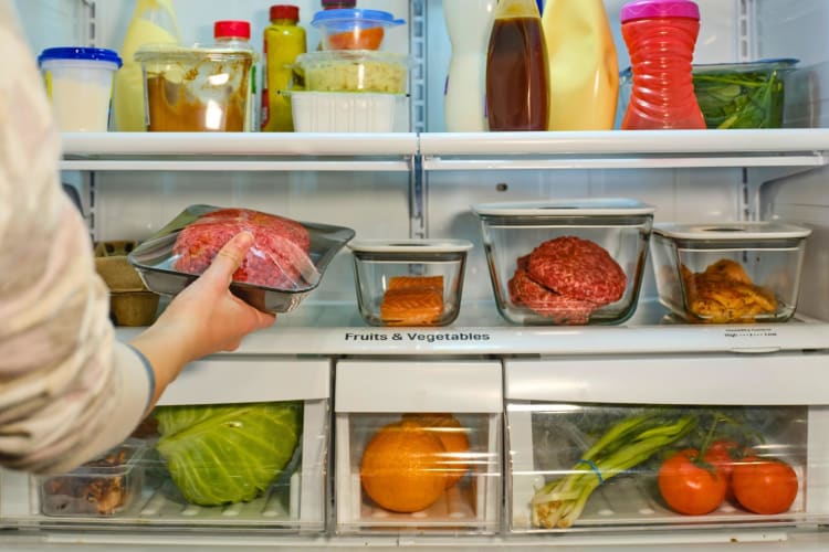 A woman putting ground beef in a refrigerator