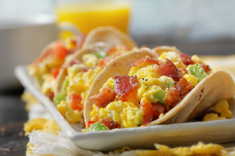 Three breakfast tacos with orange juice in the background