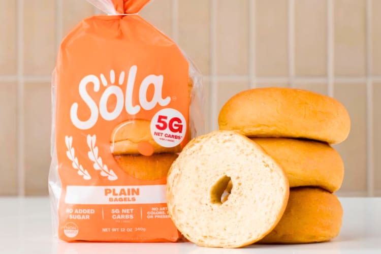 An orange bag of Sola Bread bagels next to fresh bagels