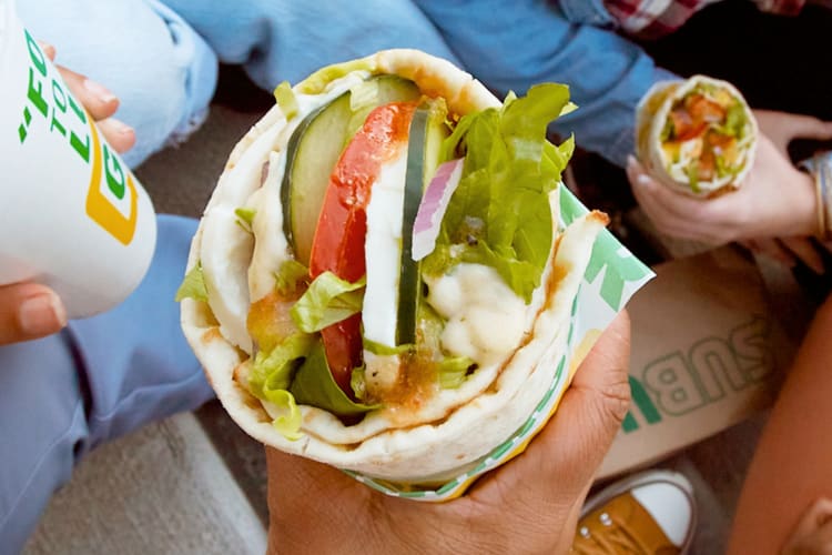 A person holding a wrap-style sandwich from Subway
