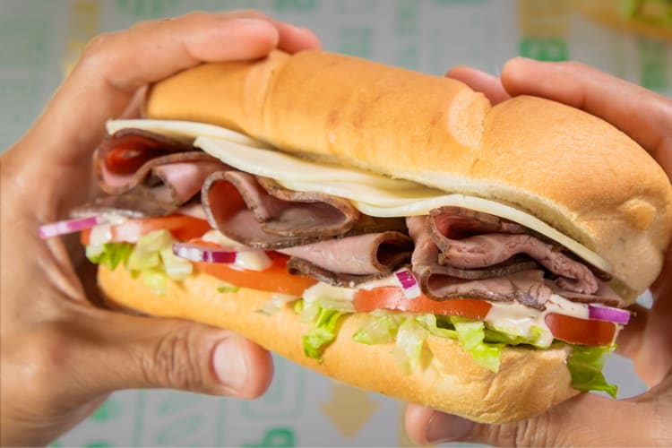 A person holding a meat and salad sandwich from Subway