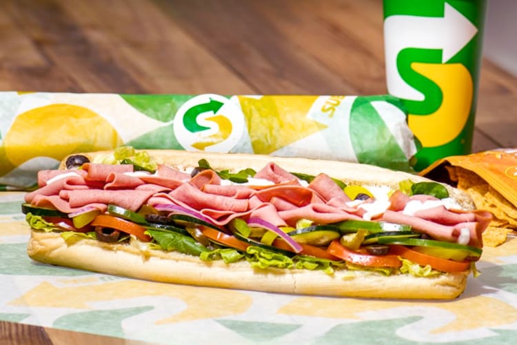 A Subway sandwich next to chips and a drink