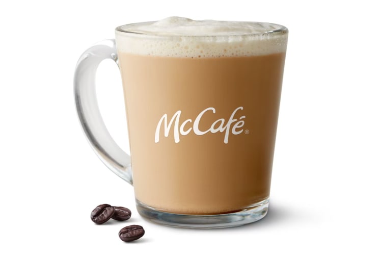 A hot McCafé Latte from McDonald's next to some coffee beans