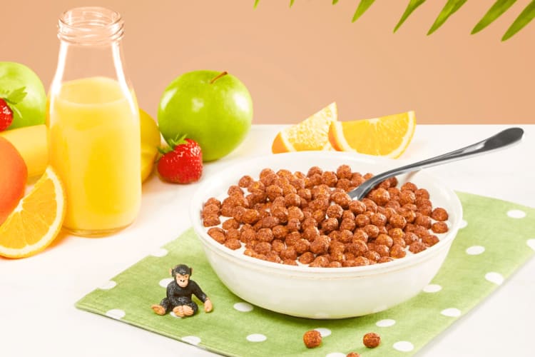 A bowl of chocolate cereal next to juice and fruit