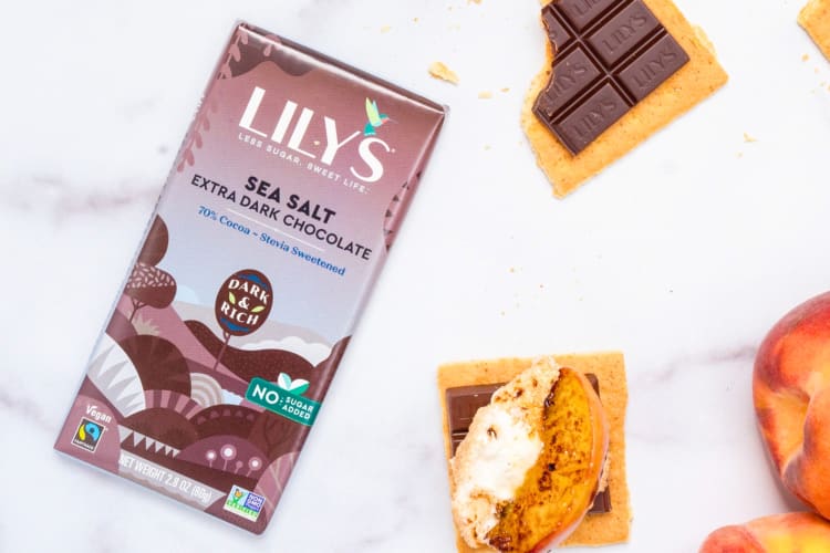 A bar of sea salt dark chocolate next to s'mores and peaches