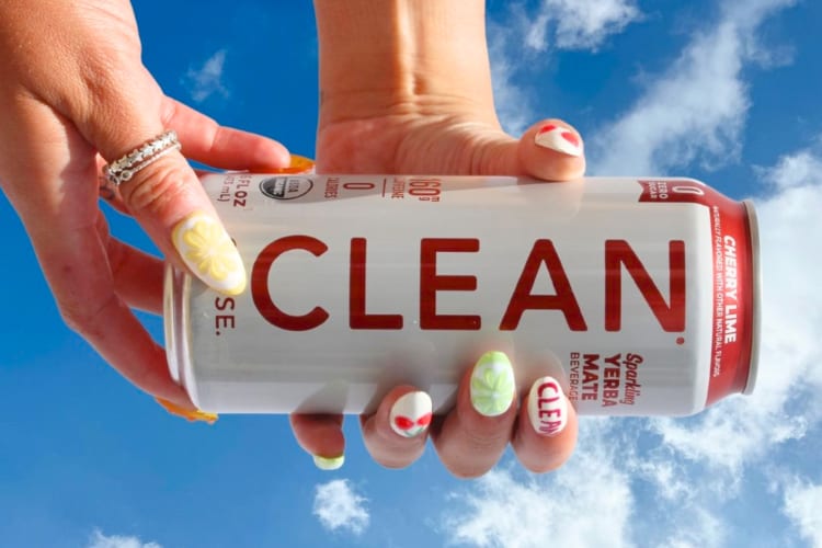 A person holding an energy drink next to blue sky with clouds