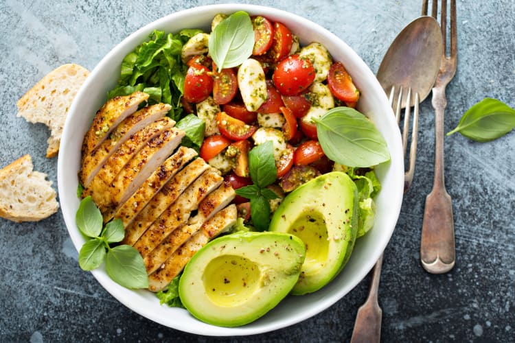 A grilled chicken salad with avocado and tomatoes