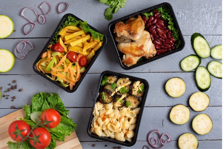 Healthy frozen meals on a table next to fresh ingredients