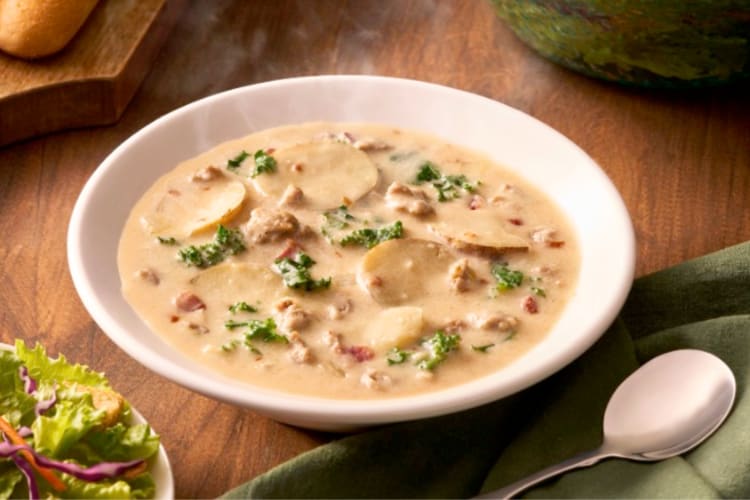 A bowl of soup next to breadsticks and salad