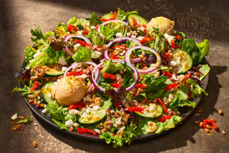 A salad bowl with greens, onions, grains and hummus