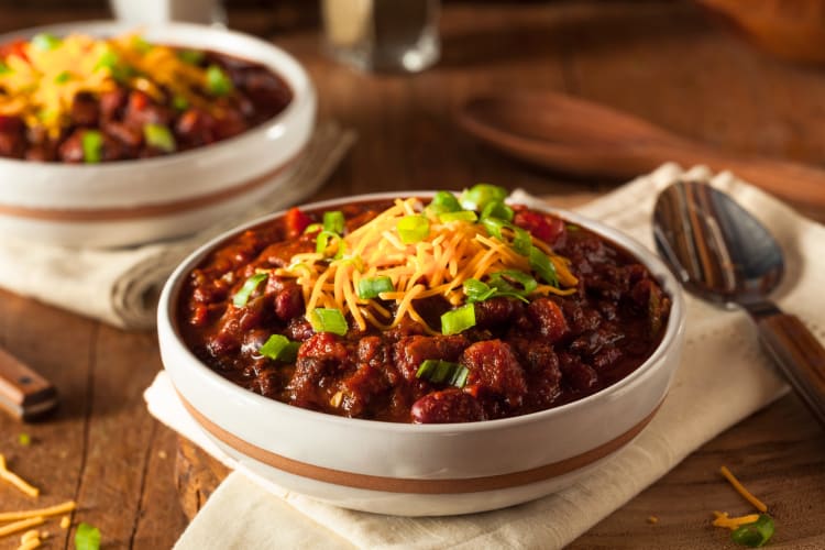 A bowl of chili with cheese and green onions