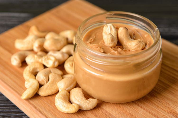 A glass jar of cashew butter with raw cashews