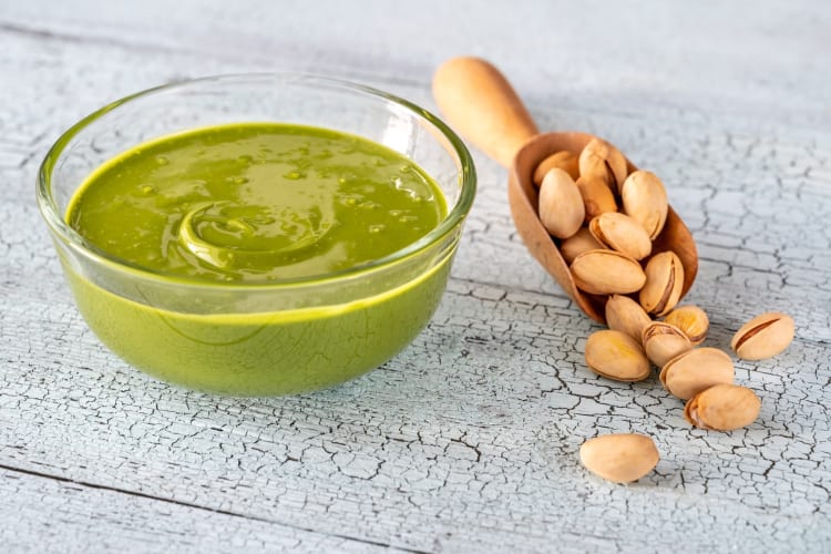 A bowl of green pistachio butter next to raw pistachios