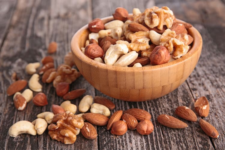 Different types of nuts in a bowl and on a wooden surface