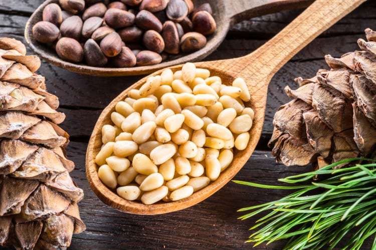 A wooden spoon with pine nuts next to a pine cone