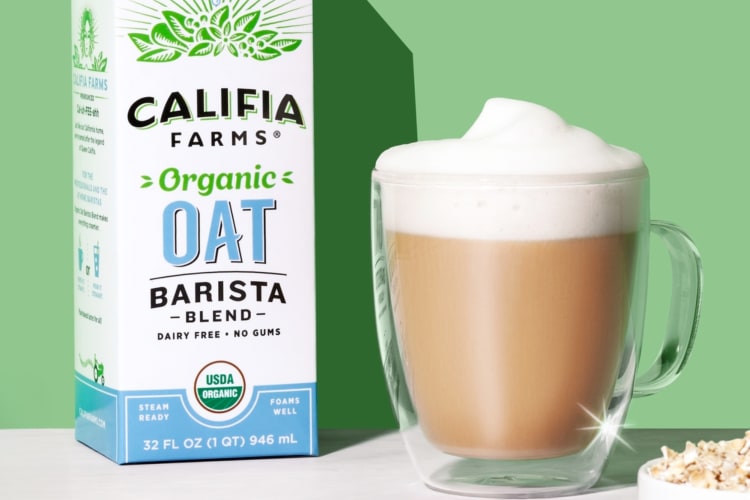 A carton of oat milk next to a coffee in a glass cup
