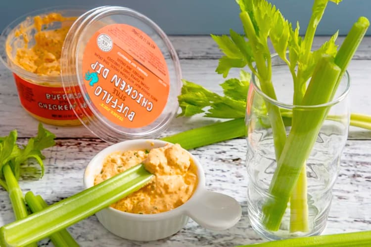 A container of Buffalo chicken dip and celery sticks