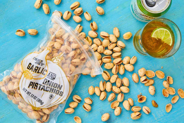 A bag of garlic and onion pistachios next to a glass of soda