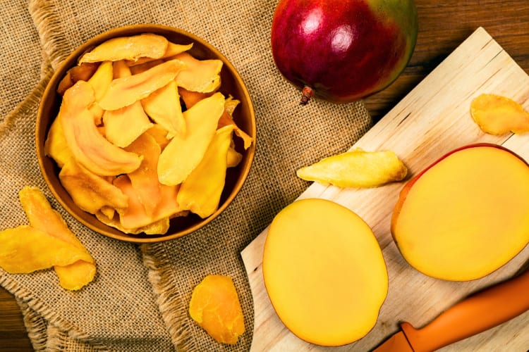 Fresh mango next to a bowl of dried mango