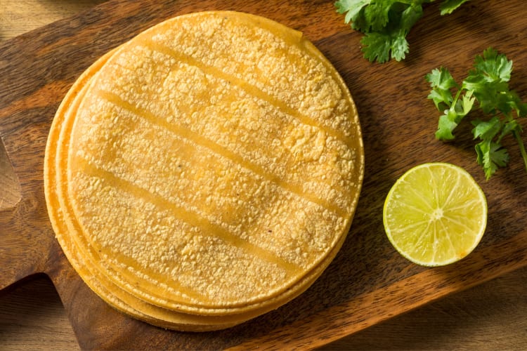 Corn tortillas on a board next to lime and cilantro