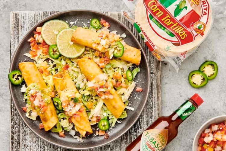 Taquitos on a plate next to a bag of corn tortillas