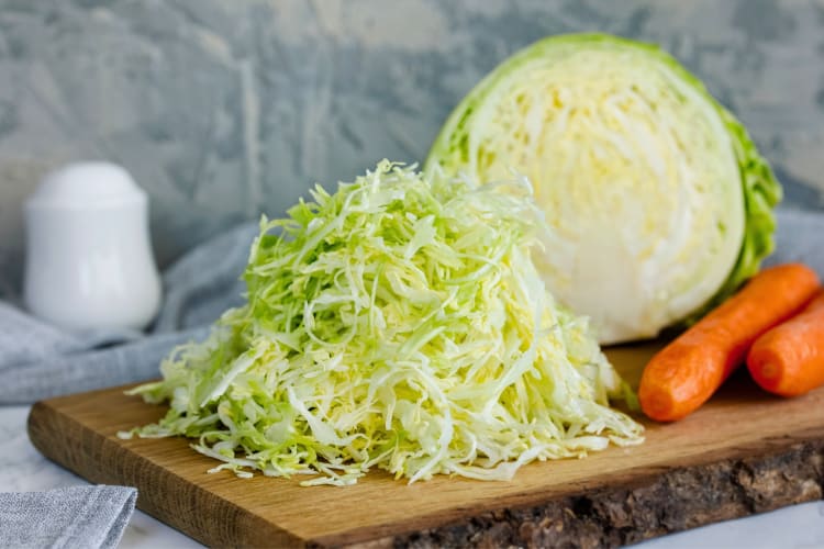 Shredded cabbage on a cutting board next to half a cabbage and carrots