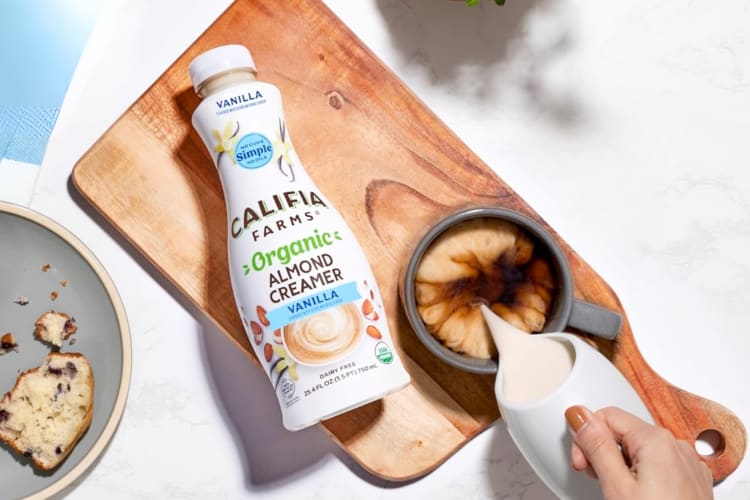 Coffee creamer on a wooden board next to cream being poured into coffee
