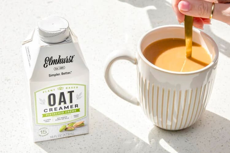 A container of pistachio coffee creamer next to a cup of coffee being stirred