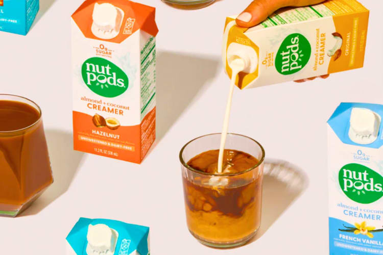 A person pouring coffee creamer into iced coffee next to other creamer bottles