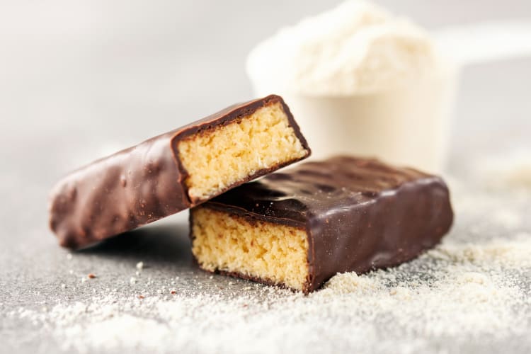 Chocolate-coated protein bars next to protein powder