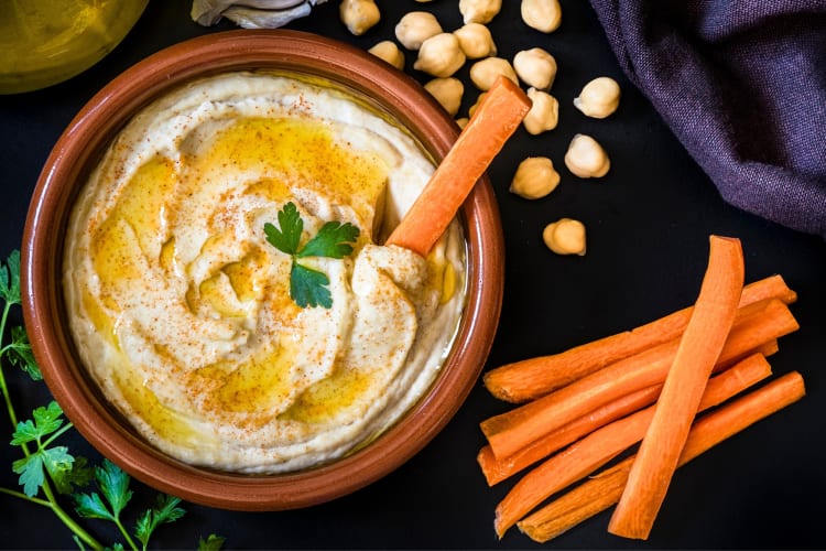 A bowl of hummus with carrot sticks
