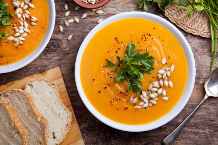 Bowls of pumpkin soup next to sliced bread