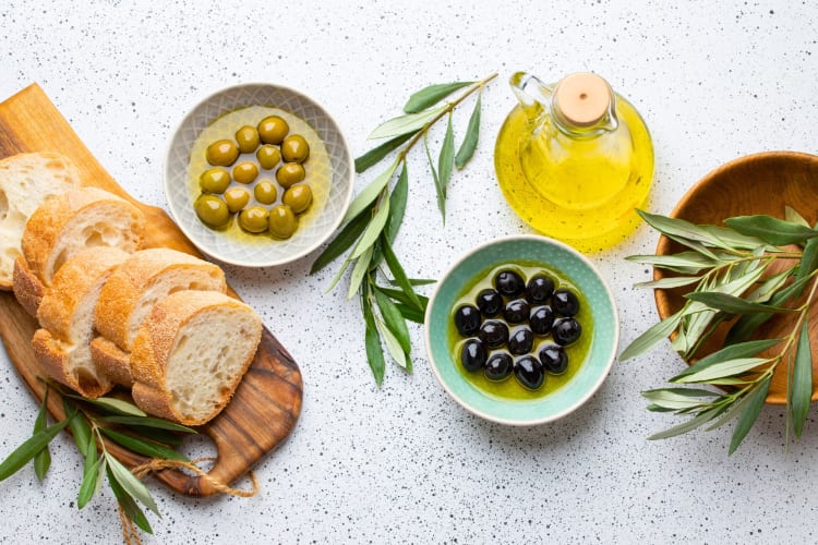 Slice bread on a board next to olives and olive oil 
