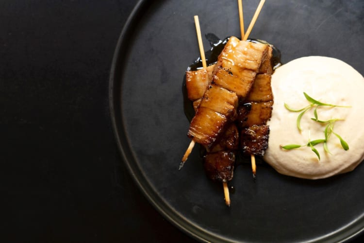 Japanese skewers on a black plate next to a sauce