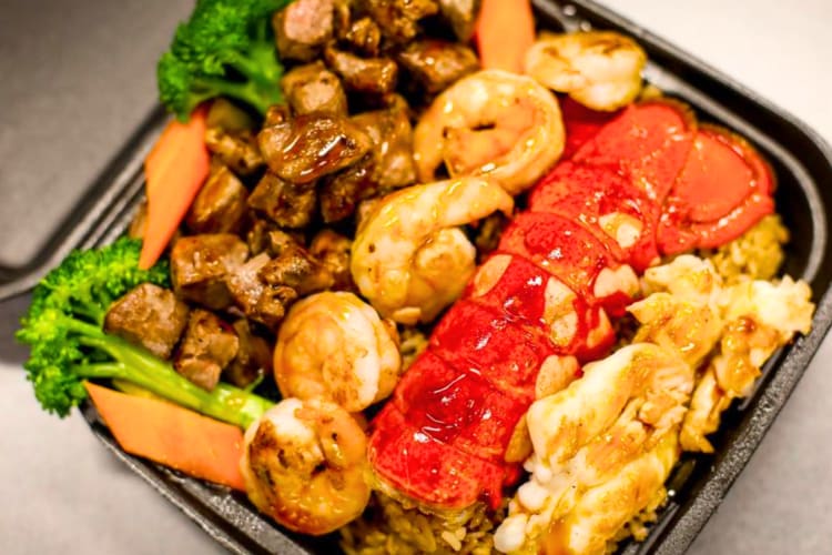 A take out box with hibachi steak, lobster, shrimp and vegetables