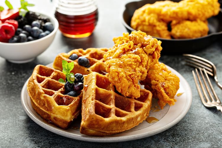 Chicken and waffles with fruit and syrup in the background