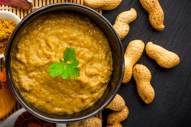 A bowl of peanut sauce next to peanuts
