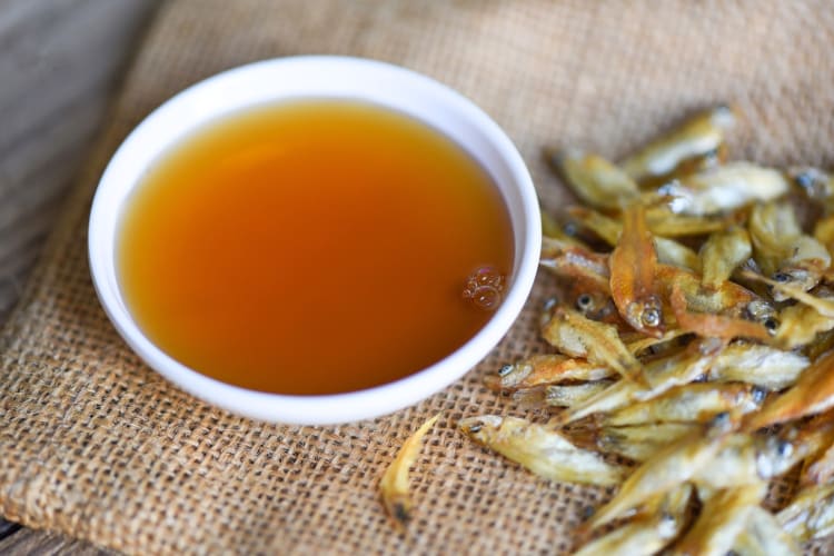 A bowl of fish sauce next to small dried fish
