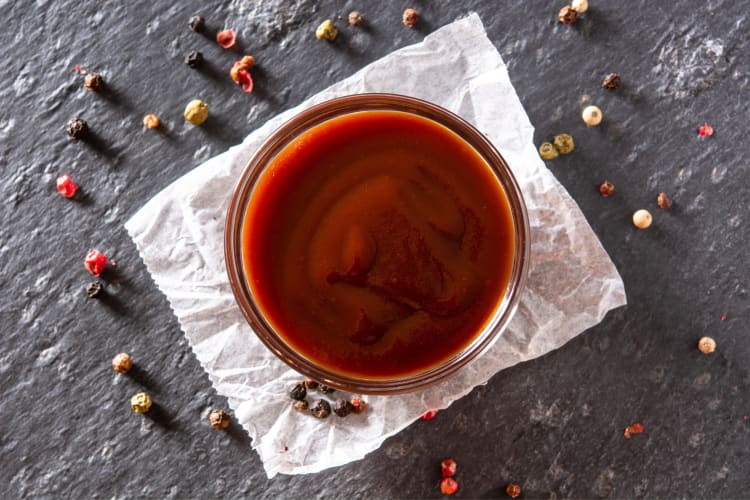 A bowl of hoisin sauce next to peppercorns
