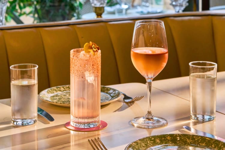 Two cocktails and two water glasses on a table next to leather booth seating