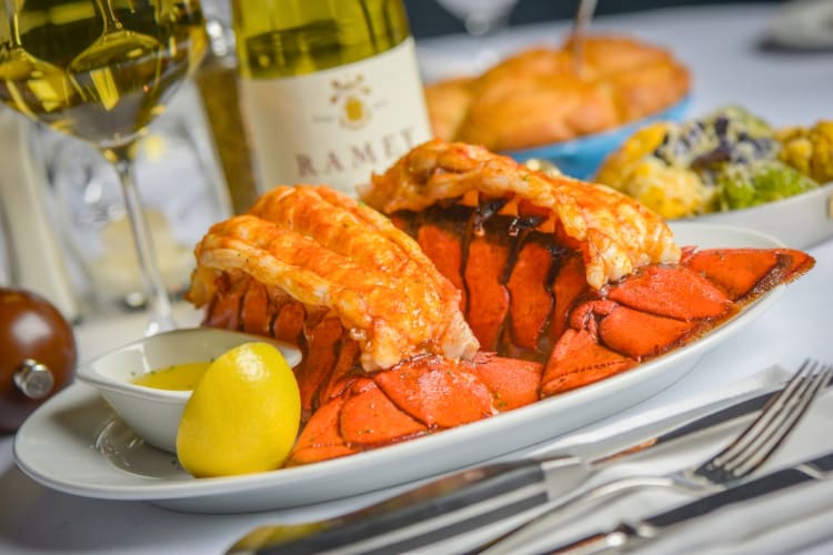 A lobser dish next to a glass and bottle of white wine
