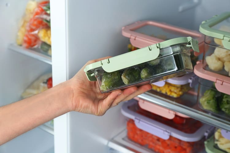 Person's hand holding a container of frozen Brussels sprouts in front on an open freezer