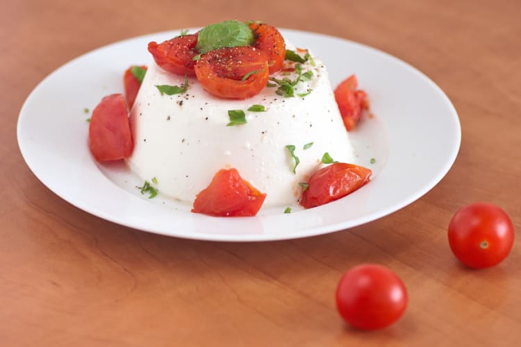 Ricotta cheese on a plate with basil leaves and cherry tomatoes